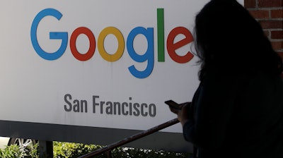 In this May 1, 2019, file photo, a woman walks past a Google sign in San Francisco. The U.S. Justice Department and the Federal Trade Commission are moving to investigate Google, Facebook, Amazon and Apple over their aggressive business practices, and the House Judiciary Committee has announced an antitrust probe of unidentified technology companies.