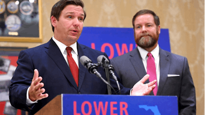 Florida Gov. Ron DeSantis speaks about the need to lower prescription costs by importing drugs from other countries, Tuesday, June 11, 2019, at the Eisenhower Recreation Center in The Villages, Fla. Listening at right is state Sen. Aaron Bean.