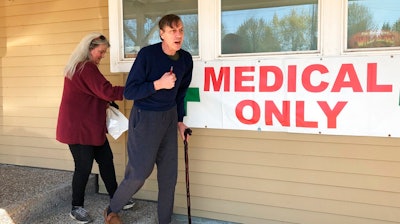 In this April 26, 2019, photo, medical marijuana cardholder Scott Donnelly, assisted by his wife and licensed caregiver, Vicki Poppen, leaves Western Oregon Dispensary in Sherwood, Ore., after buying medical marijuana to treat muscle spasms caused by his multiple sclerosis. Donnelly visits the medical-only dispensary once a week and relies on it for the cannabis that eases his tremors long enough that he can fall asleep. The dispensary is one of two medical-only shops left in Oregon.