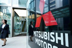 A woman walks past a sign of Mitsubishi Motors at its headquarter in Tokyo Friday, June 21, 2019. Mitsubishi Motors Corp. shareholders approved on Friday the ouster of Carlos Ghosn, who was pivotal in the Japanese automaker's three-way partnership with Nissan and Renault until he was arrested on financial misconduct charges last year.