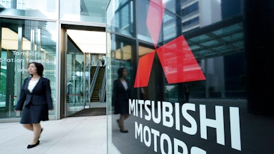 A woman walks past a sign of Mitsubishi Motors at its headquarter in Tokyo Friday, June 21, 2019. Mitsubishi Motors Corp. shareholders approved on Friday the ouster of Carlos Ghosn, who was pivotal in the Japanese automaker's three-way partnership with Nissan and Renault until he was arrested on financial misconduct charges last year.