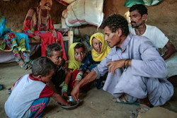 In this Oct. 1, 2018, file photo, a man feeds children halas, a climbing vine of green leaves, in Aslam, Hajjah, Yemen. The U.N. food agency has begun a partial suspension of food aid to areas of Yemen controlled by the rebels amid accusations they were diverting aid from the war-torn country's hungriest people.