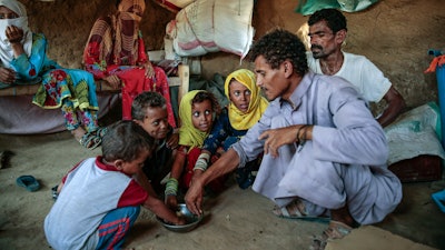In this Oct. 1, 2018, file photo, a man feeds children halas, a climbing vine of green leaves, in Aslam, Hajjah, Yemen. The U.N. food agency has begun a partial suspension of food aid to areas of Yemen controlled by the rebels amid accusations they were diverting aid from the war-torn country's hungriest people.