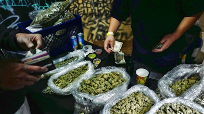 In this April 15, 2019, file photo, a vendor makes change for a marijuana customer at Rev-Up a cannabis marketplace in Los Angeles. An alliance of large cannabis businesses in the growing global marketplace has a message for the public: We're good corporate citizens. The 45-member Global Cannabis Partnership that includes Canopy Growth Corp. and other major companies issued guidelines Tuesday, June 18, 2019, aimed at minimizing greenhouse gas emissions and promoting ethical conduct and responsible pot use.