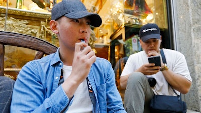 In this Monday, June 17, 2019, photo, Joshua Ni, 24, and Fritz Ramirez, 23, vape from electronic cigarettes in San Francisco. San Francisco supervisors are considering whether to move the city toward becoming the first in the United States to ban all sales of electronic cigarettes in an effort to crack down on youth vaping. The plan would ban the sale and distribution of e-cigarettes, as well as prohibit e-cigarette manufacturing on city property.
