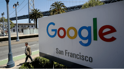 In this May 1, 2019, file photo a man walks past a Google sign outside with a span of the Bay Bridge at rear in San Francisco. Google is acquiring data analytics firm Looker for $2.6 billion cash in an effort to expand its Google Cloud business. The company says Looker will give its cloud-computing customers more ways to use their data.