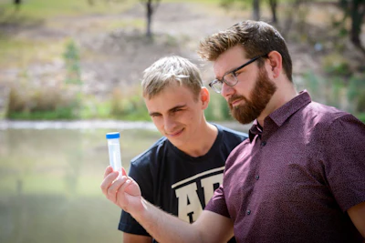 Flinders University PhD candidate Nicholas Lundquist (left) and Dr Justin Chalker (right) with a field sample of PFAS contaminated water.