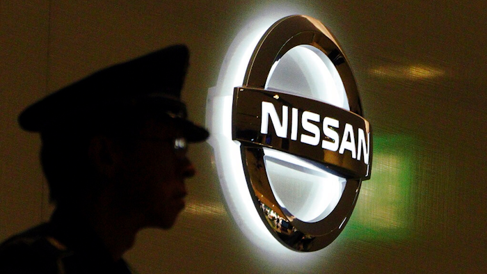 In this Nov. 21, 2018, file photo, a security guard stands near the logo at Nissan Motor Co. Global Headquarters in Yokohama near Tokyo. The executives charged with strengthening governance at Nissan are saying extensive job cuts are coming, designed to drive a recovery at the Japanese automaker.