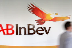 In this Thursday, March 3, 2011 file photo, a man walks past the AB InBev logos, in Leuven, Belgium. AB Inbev, the world's biggest brewer with brands like Budweiser and Corona, is selling its unit in Australia to reduce debt after it decided against listing shares in Asia. The company said Friday, July 19, 2019 it is selling Carlton & United Breweries for $16 billion AUD ($11.3 billion) to Japanese brewing rivals Asahi Group.
