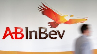 In this Thursday, March 3, 2011 file photo, a man walks past the AB InBev logos, in Leuven, Belgium. AB Inbev, the world's biggest brewer with brands like Budweiser and Corona, is selling its unit in Australia to reduce debt after it decided against listing shares in Asia. The company said Friday, July 19, 2019 it is selling Carlton & United Breweries for $16 billion AUD ($11.3 billion) to Japanese brewing rivals Asahi Group.