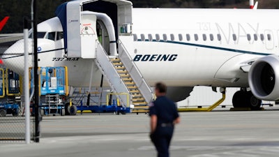 In this March 14, 2019, file photo, a worker walks next to a Boeing 737 MAX 8 airplane parked at Boeing Field in Seattle. Boeing said Thursday, July 18, it will take a $4.9 billion charge to cover possible compensation to airlines whose Max jets remain grounded after two deadly accidents.
