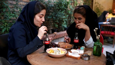 Two Iranians drink Coca-Cola at a cafe in downtown Tehran, Iran, Wednesday, July 10, 2019. Whether at upscale restaurants or corner stores, American brands like Coca-Cola and Pepsi can be seen throughout Iran despite the heightened tensions between the two countries. U.S. sanctions have taken a heavy toll, but Western food, movies, music and clothing are still widely available.