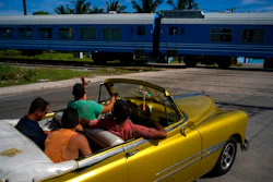 A driver in an American classic car waves as the first train using new equipment from China rides past, in Havana, Cuba, Saturday, July 13, 2019. The first train using new equipment from China pulled out of Havana Saturday, hauling passengers on the start of a 915-kilometer (516-mile) journey to the eastern end of the island as the government tries to overhaul the country’s aging and decrepit rail system.
