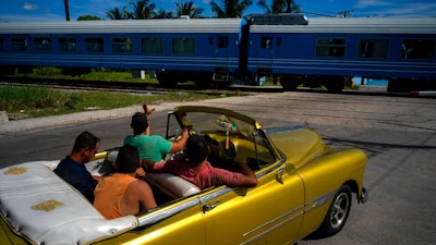 A driver in an American classic car waves as the first train using new equipment from China rides past, in Havana, Cuba, Saturday, July 13, 2019. The first train using new equipment from China pulled out of Havana Saturday, hauling passengers on the start of a 915-kilometer (516-mile) journey to the eastern end of the island as the government tries to overhaul the country’s aging and decrepit rail system.