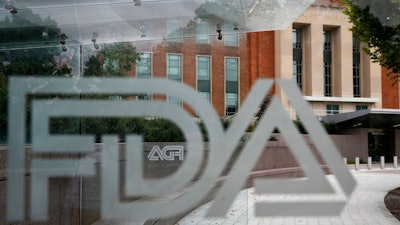 This Aug. 2, 2018, file photo shows the U.S. Food and Drug Administration building behind FDA logos at a bus stop on the agency's campus in Silver Spring, Md. The FDA has approved the first generic copies of a popular, pricey pill for nerve pain. The agency on Monday, July 22, 2019, said it approved nine generic versions of Pfizer Inc.’s Lyrica.