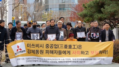 In this Nov. 29, 2018, file photo, victims of Japan's forced labor and their family members arrive at the Supreme Court in Seoul, South Korea. Colonial-era Korean laborers on Tuesday, July 16, 2019, are seeking a court's approval for the sales of local assets of their former Japanese employer after it refused to comply with a court order to compensate them for forced labor decades ago. The sign reads 'Mitsubishi Heavy Industries should compensate and apologize to victims of forced labor.'