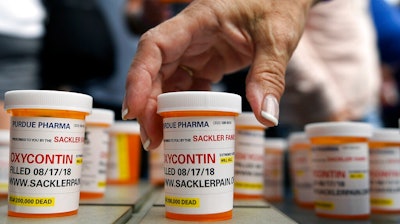 In this Aug. 17, 2018, file photo, family and friends who have lost loved ones to OxyContin and opioid overdoses leave pill bottles in protest outside the headquarters of Purdue Pharma, which is owned by the Sackler family, in Stamford, Conn. New York is suing the billionaire family behind Oxycontin, alleging the drugmaker fueled the opioid crisis by putting hunger for profits over patient safety.