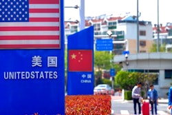 In this May 8, 2019, photo, people walk by a display boards featuring the U.S. and Chinese flags in a special trade zone in Qingdao in eastern China's Shandong province. A government spokesman says Chinese companies have expressed willingness to import U.S. farm goods as envoys prepare to meet next week for talks aimed at ending a tariff war.