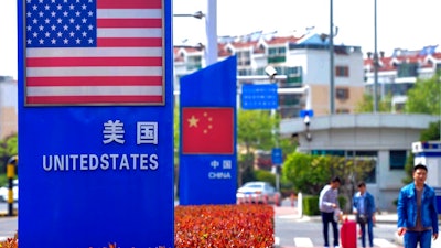In this May 8, 2019, photo, people walk by a display boards featuring the U.S. and Chinese flags in a special trade zone in Qingdao in eastern China's Shandong province. A government spokesman says Chinese companies have expressed willingness to import U.S. farm goods as envoys prepare to meet next week for talks aimed at ending a tariff war.