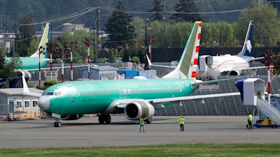In this Wednesday, May 8, 2019 file photo, workers stand near a Boeing 737 MAX 8 jetliner being built for American Airlines prior to a test flight in Renton, Wash. Federal safety officials are recruiting pilots from airlines around the world to test changes that Boeing is making in flight-control software on the grounded 737 Max jet, according to two people briefed on the situation