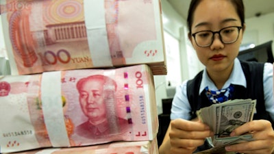 A bank employee counts U.S. dollar banknotes next to stack of 100 Chinese yuan notes at a bank outlet in Hai'an in eastern China's Jiangsu province, Tuesday, Aug. 6, 2019. China's yuan fell further Tuesday against the U.S. dollar, fueling fears about increasing global damage from Beijing's trade war with President Donald Trump.