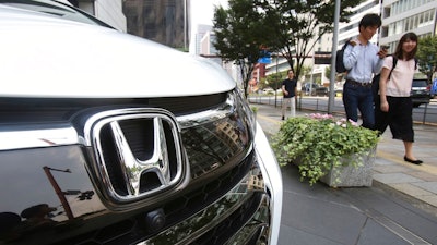 In this July 31, 2019, photo, people walk past a Honda car on display at Honda Motor Co. headquarters in Tokyo. Japanese automaker Honda reported Friday, Aug. 2, a 29% decline in fiscal first quarter profit as an unfavorable currency exchange and declining auto sales in the U.S. and India hurt earnings.