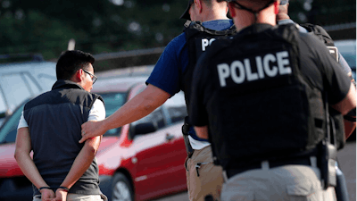 In this Aug. 7, 2019, file photo, a man is taken into custody at a Koch Foods Inc. plant in Morton, Miss. Unauthorized workers are jailed or deported, while the managers and business owners who profit from their labor often aren't. Under President Donald Trump, the numbers of owners and managers facing criminal charges for employing unauthorized workers have stayed almost the same.