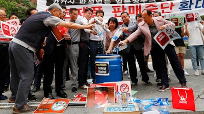 In this July 15 2019, photo, South Korean small and medium-sized business owners pour beers and drinking waters from Japanese brands into a trash can during a rally calling for a boycott of Japanese products in front of the Japanese embassy in Seoul, South Korea, The signs read: 'Our supermarket does not sell Japanese products.' A widespread anti-Japanese boycott has gained ground in South Korea since Tokyo tightened its exports of materials used to manufacture semiconductors and display screens, key export items for South Korea.