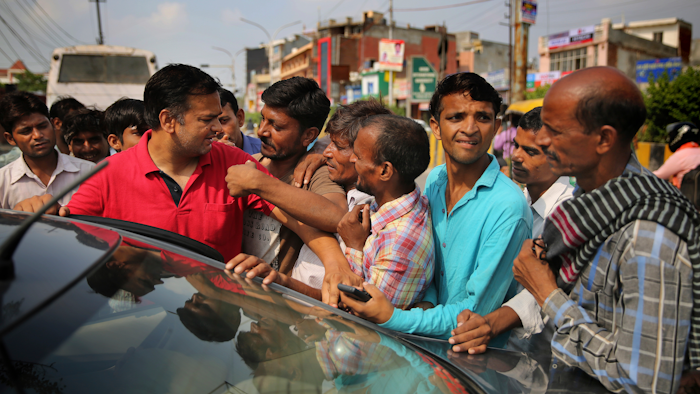 In this photo, Indian daily wage laborers and construction workers jostle as a man, in red shirt, tries to hire them, on the outskirts of New Delhi, India.