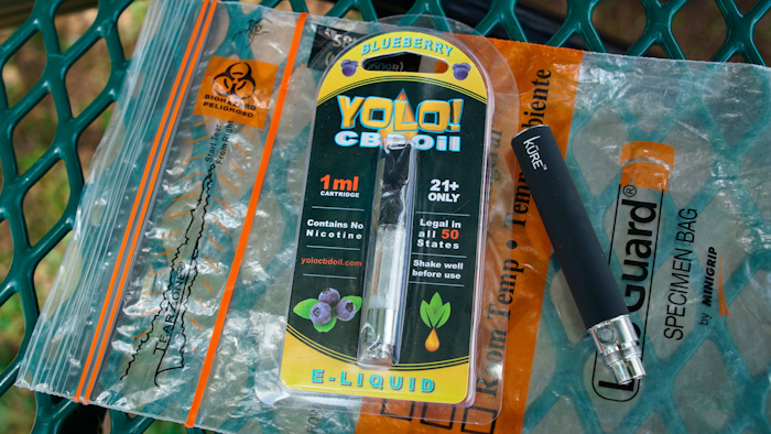 A Yolo! brand CBD oil vape cartridge sits alongside a vape pen on a biohazard bag. Jay Jenkins says two hits from the vape put him in a coma and nearly killed him in 2018.