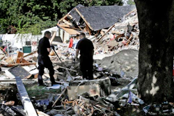 In this Sep. 21, 2018, file photo, fire investigators pause while searching the debris at a home which exploded following a gas line failure in Lawrence, Mass. Federal officials are discussing their findings from a yearlong investigation into last September's natural gas explosions and fires in Massachusetts. The National Transportation Safety Board meets in Washington, D.C., on Tuesday, Sept. 24, 2019, to discuss and vote on its final report about the Sept. 13, 2018, incident.