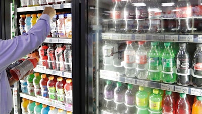 In this Monday, Oct. 1, 2018 file photo, a shop owner reaches into a drink display refrigerator at his convenience store in Kent, Wash. A study on America’s eating habits released on Tuesday, Sept. 24, 2019 shows only slight improvement from 1999 to 2016. While adults cut down a bit on added sugars and ate marginally more whole grains, they still eat too many sweetened foods and unhealthy fats.