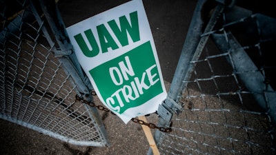 In this Monday, Sept. 16, 2019, file photo, a United Auto Workers strike sign rests between the chains of a locked gate entrance outside of Flint Engine Operations in Flint, Mich. As the United Auto Workers’ strike against General Motors continues, consumers, the company and striking workers are starting to get pinched.