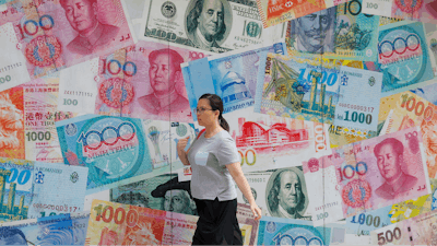 In this Aug. 6, 2019, file photo, a woman walks by a money exchange shop decorated with different countries currency banknotes at Central, a business district in Hong Kong. China has urged President Donald Trump to oppose bullying following the American leader’s criticism of its trade status in a speech at the United Nations. A foreign ministry spokesman on Wednesday, Sept. 25, called on Trump to “meet China halfway” in settling trade disputes.