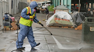 In this file photo, a city worker uses a power washer to clean the sidewalk by a tent city along Division Street in San Francisco..