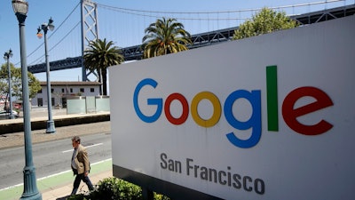 In this May 1, 2019, file photo a man walks past a Google sign outside with a span of the Bay Bridge at rear in San Francisco. A group of states are expected to announce an investigation into Google on Monday, Sept. 9, to investigate whether the tech company has become too big.