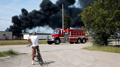 A resident watches as a firetruck arrives in downtown Dupo, Ill. to help fight a tanker fire from a derailed train on Tuesday, Sept. 10. 2019. Black smoke coming from the derailment scene can be seen for miles and caused the evacuation of schools in the town, authorities said.