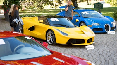 People looking at a Aston Martin One-77 Coupe (2011) in front of a Ferrari LaFerrari (2015), yellow, and a Bugatti Veyron EB 16.4 Coupe (2010), blue, part of some 25 luxury cars owned by Teodoro Obiang, the son of the Equatorial Guinea's President Teodoro Obiang Nguema Mbasogo are pictured before an auction of sales house Bonhams at the Bonmont Abbey Golf & Country Club in Cheserex near Geneva, Switzerland, Sunday, Sept. 29, 2019. A collection of luxury cars from Equatorial Guinea's vice president Teodorin Obiang Nguema confiscated by the Geneva prosecutor's office after a deal ending a money-laundering inquiry, are auctioned off in Switzerland and are estimated to bring in 18.5 million Swiss francs.