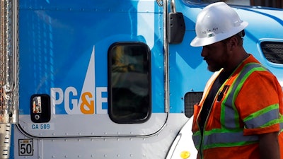 In this Aug. 15, 2019, file photo, a Pacific Gas & Electric worker walks in front of a truck in San Francisco. Pacific Gas & Electric and a group of insurers say they have reached an $11 billion settlement to cover most of the claims from the 2017 and 2018 wildfires in California. The utility said in a statement Friday, Sept. 13, that the tentative agreement covers 85% of the insurance claims, including a fire that decimated the town of Paradise.