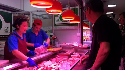 In this photo, clerks help a customer shop for pork at a meat market in Beijing.