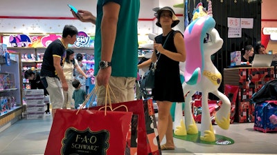 In this June 1, 2019, photo, file a man carries a paper bags containing toys purchased from the FAO Schwarz as people shop at the newly open FAO Schwarz toy store at the capital city's popular shopping mall in Beijing. Caught in the crossfire of a trade war, American businesses operating in the China say they’ve been hurt by the hostilities between the world’s two biggest economies and are facing increasingly unfair competition from Chinese firms.