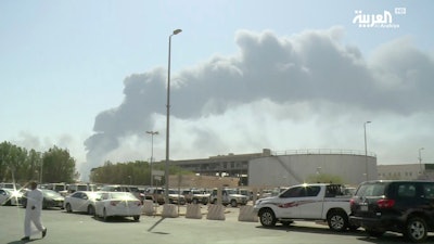 In this image made from a video broadcast on the Saudi-owned Al-Arabiya satellite news channel on September 14, 2019, a man walks through a parking lot as the smoke from a fire at the Abqaiq oil processing facility can be seen behind him in Buqyaq, Saudi Arabia.