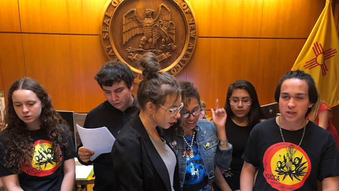 High school student Artemisio Romero y Carver, right, of Santa Fe, leads environmental activists in a climate change protest song as they deliver a letter of demands to the office of New Mexico Gov. Michelle Lujan Grisham.