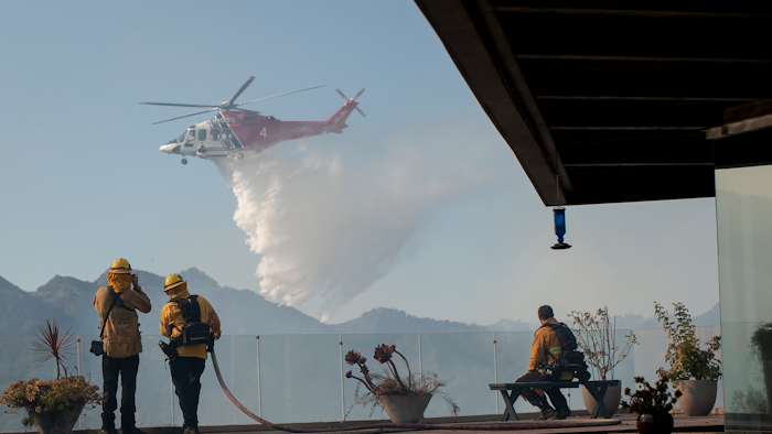 Firefighters watch as a helicopter drops water in a wildfire in the Pacific Palisades area of Los Angeles.