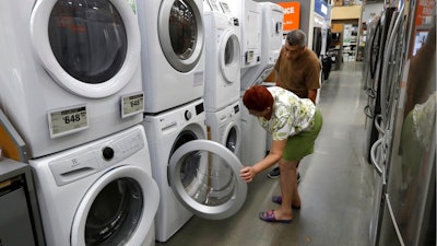 In this Monday, Sept. 23, 2019 photo Maria Alvarez, front, and her husband Guillermo Alvarez, behind, both of Boston, examine clothes washers and dryers at a Home Depot store location, in Boston. On Thursday, Oct. 24, the Commerce Department releases its September report on durable goods.