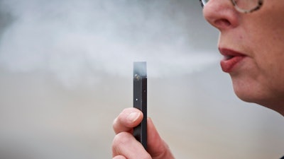 In this April 16, 2019, file photo, a woman exhales a puff of vapor from a Juul pen in Vancouver, Wash. A former Juul Labs executive is alleging that the vaping company knowingly shipped 1 million tainted nicotine pods to customers. The allegation comes in a lawsuit filed Tuesday, Oct. 29, by a former finance executive who was fired by the vaping giant earlier this year.