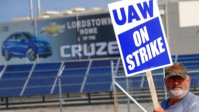 In this Sept. 16, 2019, file photo a picketer carries sign at one of the gates outside the closed General Motors automobile assembly plant in Lordstown, Ohio. A tentative four year contract with striking General Motors gives workers a mix of pay raises, lump sum payments and an $11,000 signing bonus. In return, the contract allows GM to proceed with factory closures in Lordstown, Ohio, Warren, Mich., and near Baltimore.