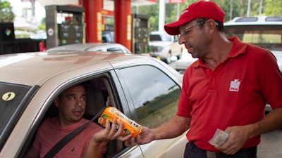 Gas station attendant Orlando Godoy takes a package of corn flour as payment after filling a motorist's tank in San Antonio de los Altos on the outskirts of Caracas, Venezuela.