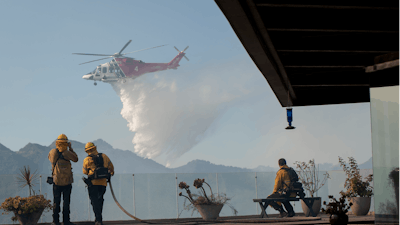 Firefighters watch as a helicopter drops water in a wildfire in the Pacific Palisades area of Los Angeles.