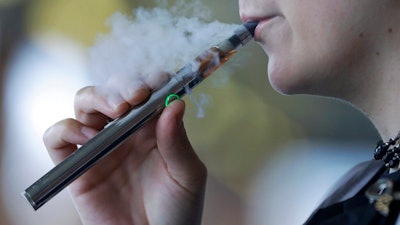 In this Friday, Oct. 4, 2019, file photo, a woman using an electronic cigarette exhales in Mayfield Heights, Ohio. A Michigan judge is blocking the state's two-week-old ban on flavored e-cigarettes. Court of Claims Judge Cynthia Stephens issued a preliminary injunction Tuesday, Oct. 15, 2019. She says Michigan Gov. Gretchen Whitmer's administration's delay in implementing the ban undercut its position that emergency rules were needed.